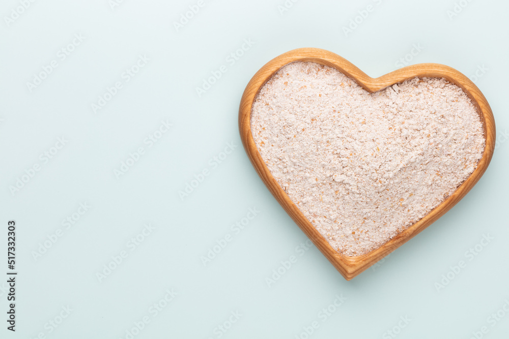 Wheat flour in a wooden heart shape bowl on a pastel background. Wheat flour in a wooden heart shape bowl on a pastel background.