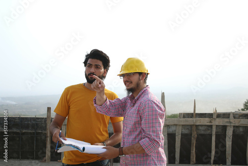 Two engineers standing at construction site looking at blueprints