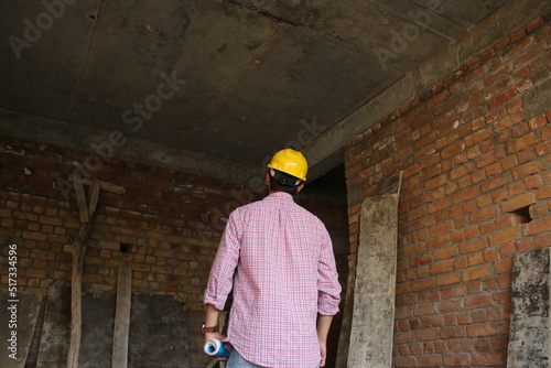 Young engineer wearing yellow safety helmet looking at blueprints in house at construction site