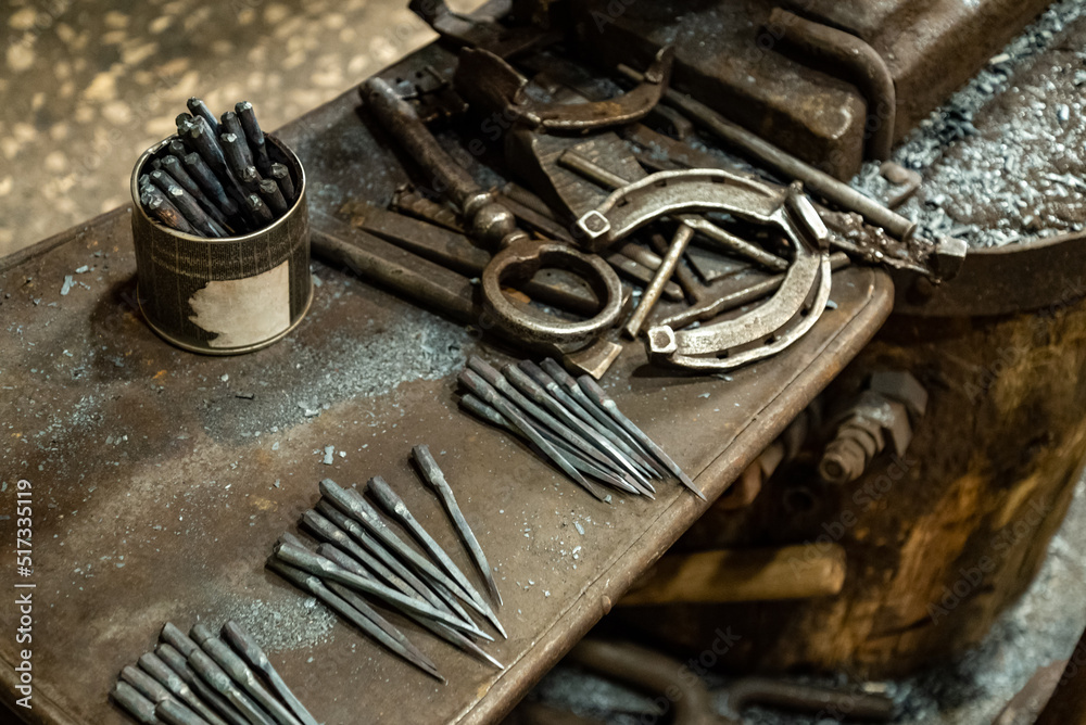 Working tools, nails and metal horseshoe on table surface in blacksmith shop Working tools, nails and metal horseshoe on table surface in blacksmith shop