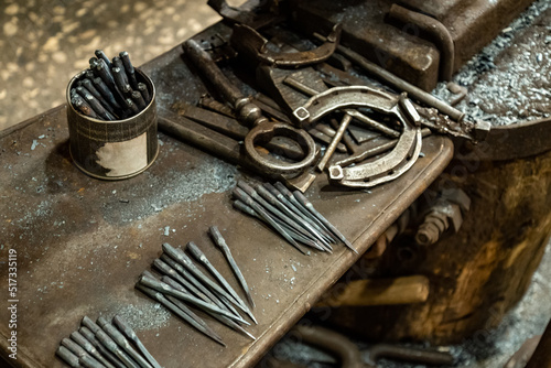 Working tools, nails and metal horseshoe on table surface in blacksmith shop