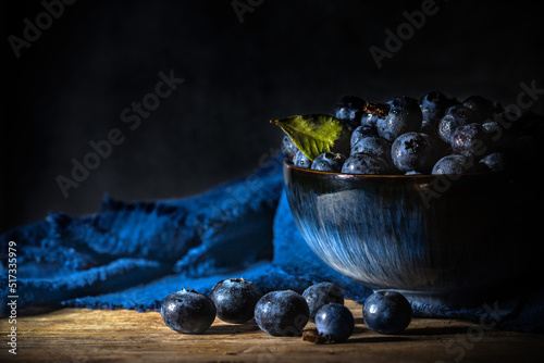 Blueberries in a blue bowl with napkin on wooden board table and background - dark and moody