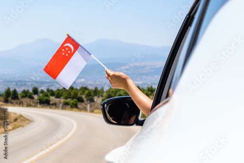 Woman holding Singapore flag from the open car window driving along the serpentine road in the mountains. Concept photo