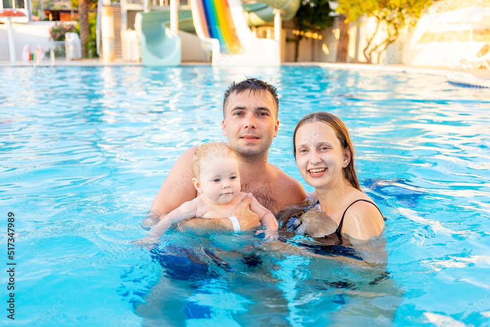 happy family mom, dad and baby daughter are swimming in the pool with water slides and having fun on vacation
