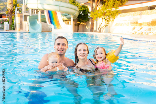 happy family mom, dad and two children are swimming in the pool with water slides and having fun on vacation, smiling and laughing