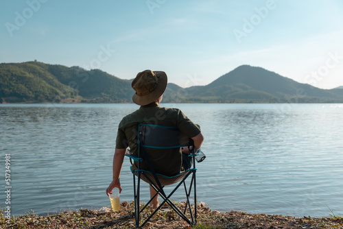The man relax on vacation with beer and sit at champing chair among lake and mountain view, Thailand