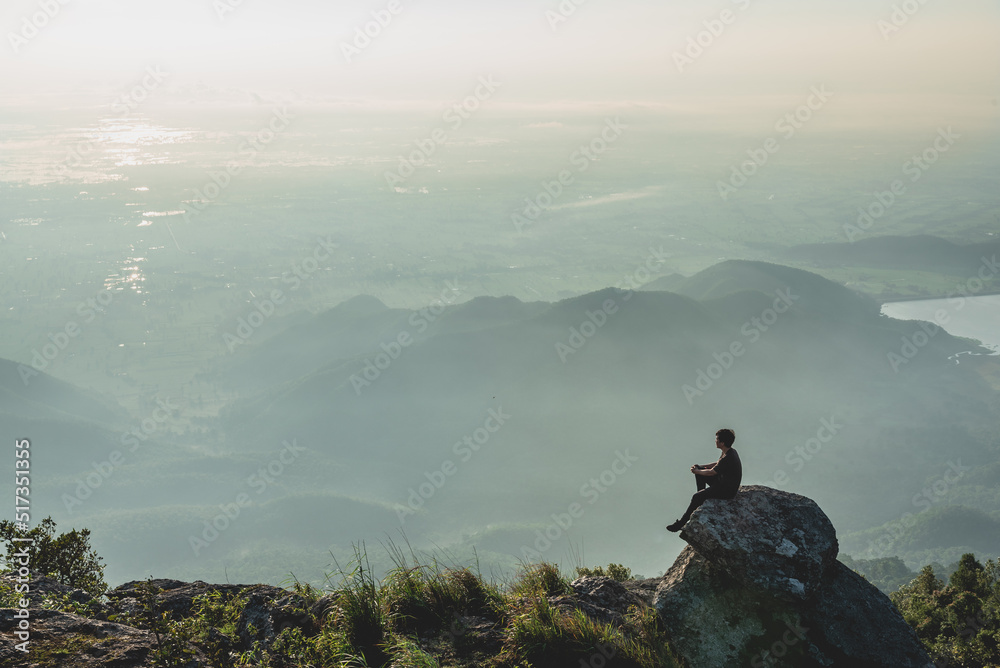 A traveling man sit on the big rock to see sunset and mountain view for relaxation