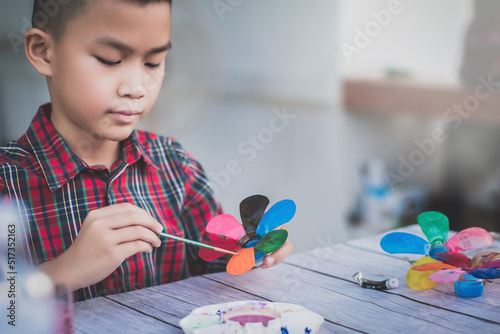 Asian boy painting a colourful plastic flower made from water bottle on wooden table outdoor.Recycled colorful plastic flowers.Recycle decoration.