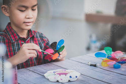Asian boy painting a colourful plastic flower made from water bottle on wooden table outdoor.Recycled colorful plastic flowers.Recycle decoration.