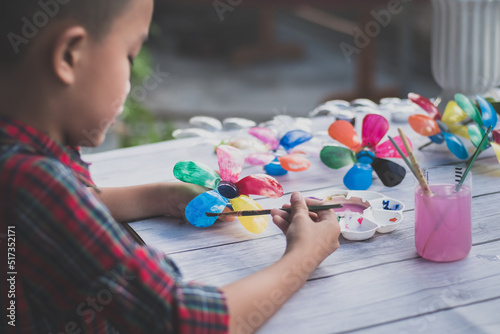 Asian boy painting a colourful plastic flower made from water bottle on wooden table outdoor.Recycled colorful plastic flowers.Recycle decoration.