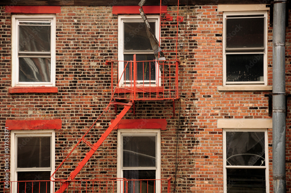 The exterior of a red brick building as a metal fire escape is located near one of the windows in New York City. The exterior of a red brick building as a metal fire escape is located near one of the windows in New York City.