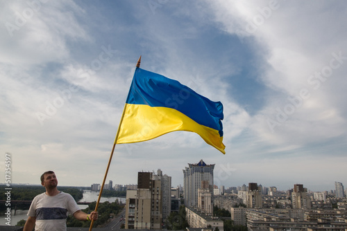 Ukrainian flag in the hands of a man standing on the roof of a house in Kyiv above the buildings. National symbol of freedom and independence. stop the war. Solidarity, expectation of victory, faith