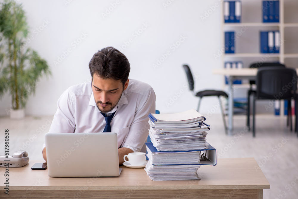 Young male employee unhappy with excessive work in the office Young male employee unhappy with excessive work in the office