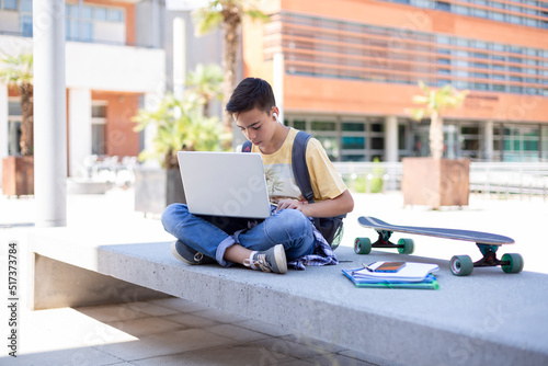 Caucasian boy high school student using laptop computer outdoors. Space for text.