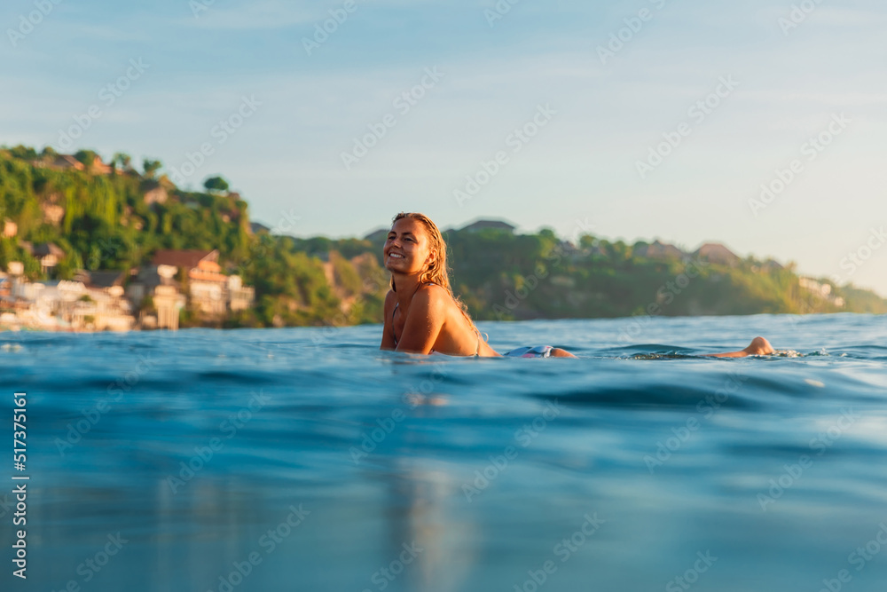 Happy surfer woman on surfboard in ocean and amazing landscape on background.
