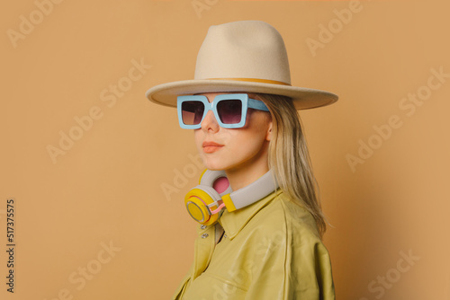 Stylish 80s woman in eyeglasses, headphones and hat on brown background © Masson