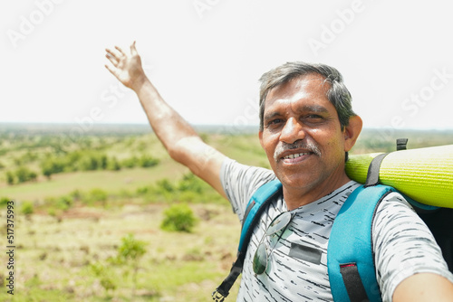Muddle aged travel vlogger with backpack talking to camera by holding it on top of hill - concept of content creater, hiking and freedom photo