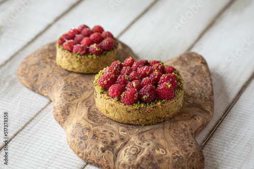 Two delicious raspberry tartlets with pistachios on wooden background