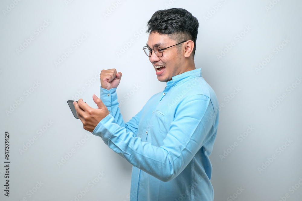 Shocked young good looking Asian man using smartphone to read good news online Shocked young good looking Asian man using smartphone to read good news online