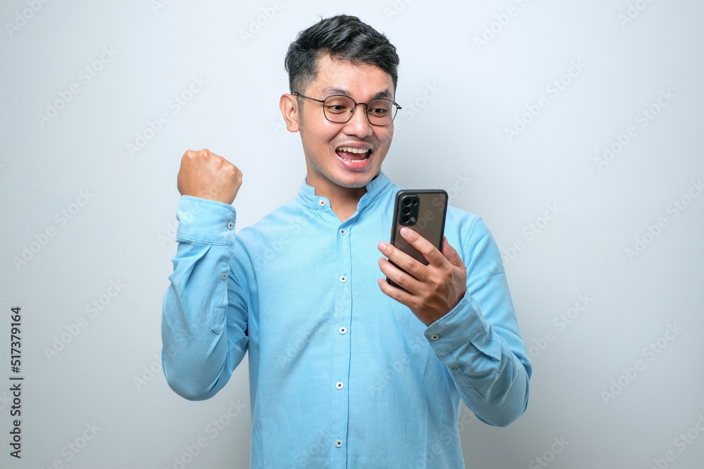 Shocked young good looking Asian man using smartphone to read good news online Shocked young good looking Asian man using smartphone to read good news online