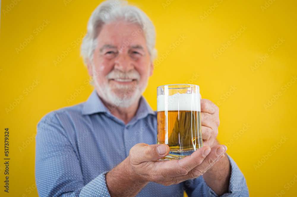 Handsome happy senior man holding a glass of fresh blonde beer - caucasian bearded elderly man on yellow background Handsome happy senior man holding a glass of fresh blonde beer - caucasian bearded elderly man on yellow background