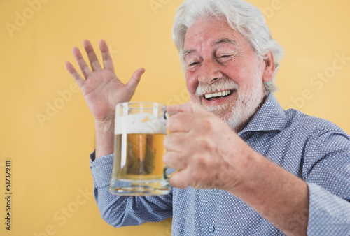 Handsome happy senior man appreciating a glass of fresh blonde beer - caucasian bearded elderly man on yellow background