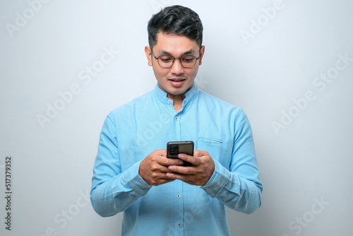 Smiling young good looking Asian man using smartphone to get in touch with family and friends isolated