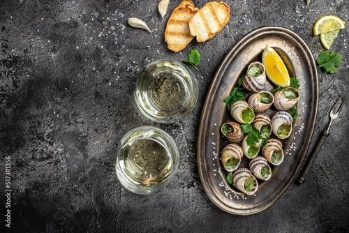 Delicious cooked sea escargo snails with herbs  butter  garlic on metal plate with forks. wine glass. gourmet food. Restaurant menu  Traditional French cuisine