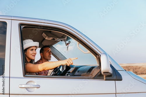 Young couple consisting of boy and girl traveling in their camper van prepared for road trips. The woman indicates the way to follow to the man with her hand. Van life concept.