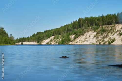 Blue lake and green mixed forest on a sunny summer day. Girvas paleovolcano is popular place among tourists. The concept of travel in Russia. Blurred surface of water is long exposure. photo