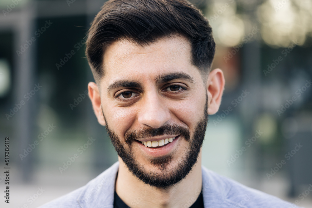 Face portrait of attractive joyful young caucasian mixed race man in business formal suit smiling and posing near modern buildings outside. Businessman. Ethnicity Face portrait of attractive joyful young caucasian mixed race man in business formal suit smiling and posing near modern buildings outside. Businessman. Ethnicity