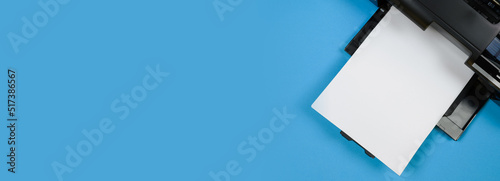 Top view of the printer and a blank sheet of a4 paper on a blue background.Banner