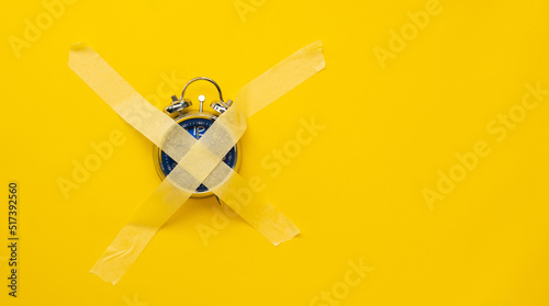 Blue clock sticked up crosswise with masking tape isolated on yellow background with copy space. Concept of timeless things in life, deficiency of time. Weekend morning without work hours photo