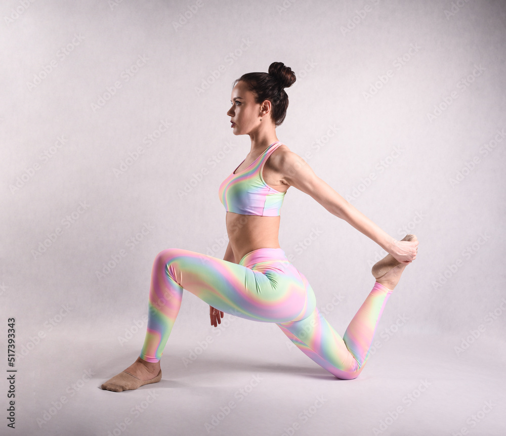 Fototapeta premium A beautiful slender gymnast in a stretch in a tracksuit does sports or yoga in the studio