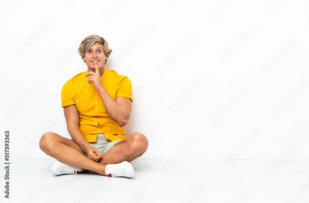 Young English man sitting on the floor showing a sign of silence gesture putting finger in mouth Young English man sitting on the floor showing a sign of silence gesture putting finger in mouth