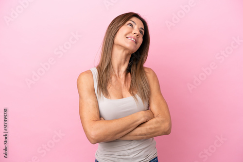Middle age caucasian woman isolated on pink background looking up while smiling