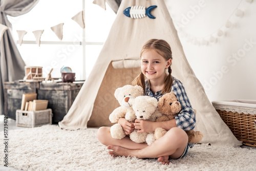 Little girl hugging plush teddies and smiling at camera in playroom