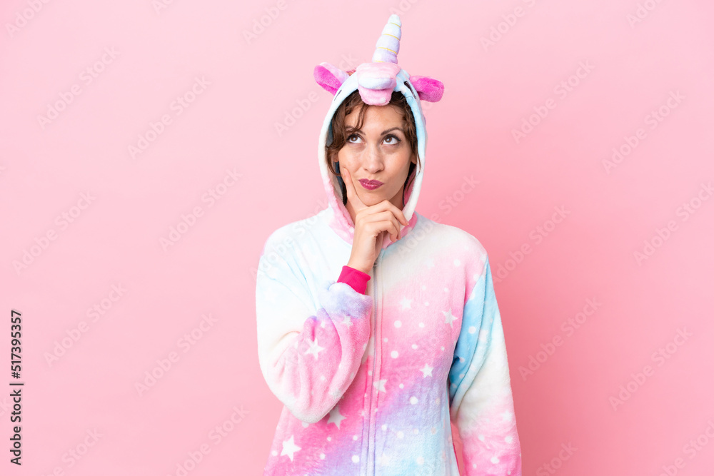 Young caucasian woman with unicorn pajamas isolated on pink background having doubts and with confuse face expression