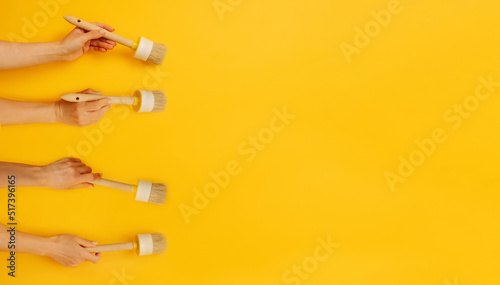 Four hands holding paint brushes on yellow background with copy space. Concept of creativity, improvement and inspiration. Working tool equipment for brushing