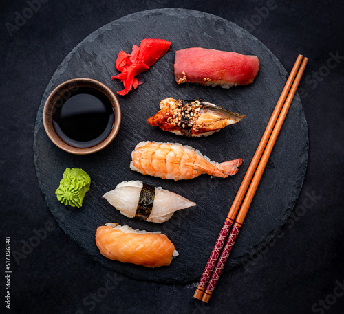 Beautiful japanese sushi sashimi set composition with shrimps, ginger and soy sauce served with chopsticks and green wasabi on black table from above. Traditional asian food with rice and seafood