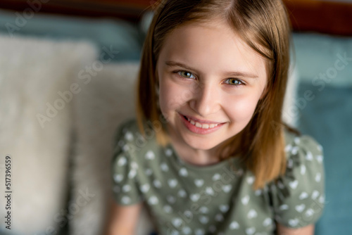 Closeup portrait og cute preteen kid girl looking at the camera and smiling. Little schoolgirl model with pretty face in the bedroom photo