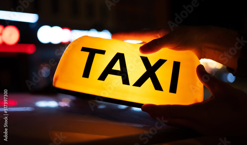 Taxi car neon light on dark street at night illuminates. Cab sign on the vehicle transportation roof glowing in the dusk