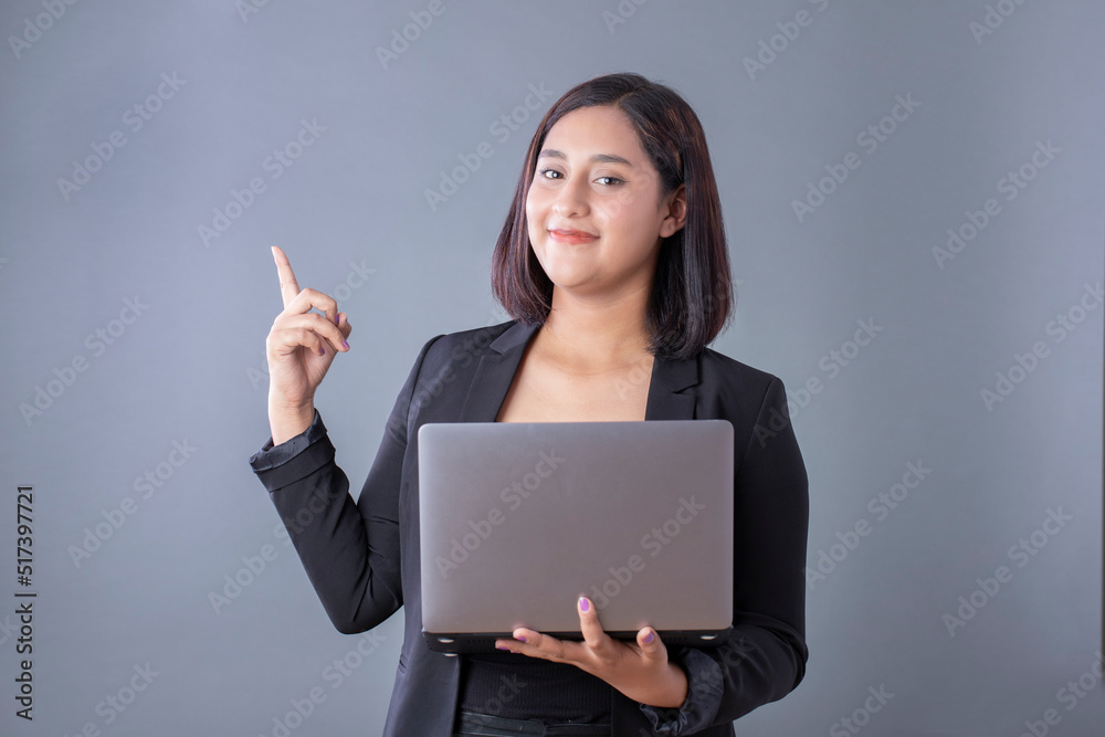 Mexican woman smiling holding laptop and pointing on gray background Mexican woman smiling holding laptop and pointing on gray background