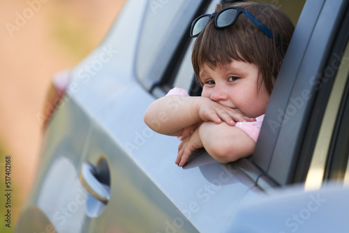 A bored little girl in the back window of a car. The child's fatigue from a long journey or sadness about saying goodbye to the sea. Selective focus. photo