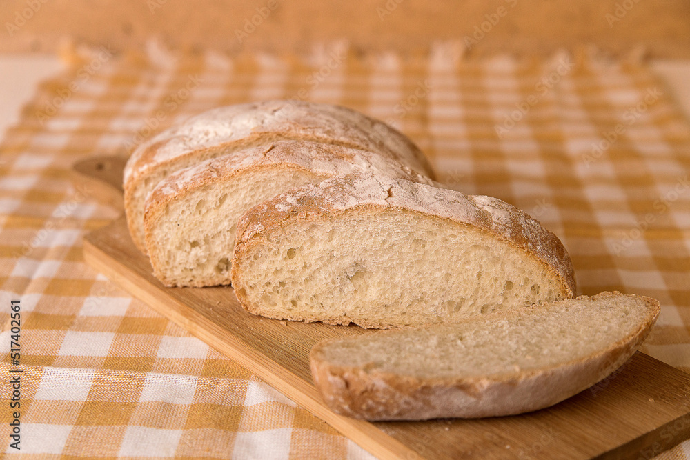 Fresh chabata bread cut into pieces on a wooden board, yellow towel, minimalism