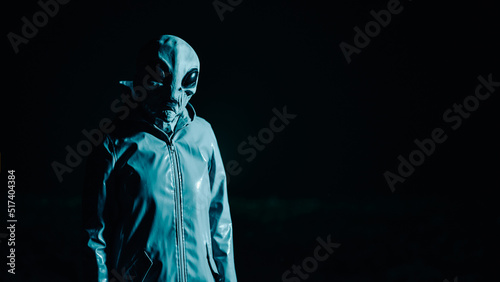 Portrait of spooky alien in dark black background. Scary mask, vinyl smooth raincoat. UFO, extraterrestrial life, halloween cosplay concept.