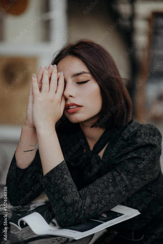 a brunette girl in a short dark dress and black glasses sits on a chair in a cafe in the city a brunette girl in a short dark dress and black glasses sits on a chair in a cafe in the city