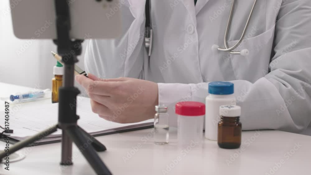 doctor hands holding pen in hands while talking on camera mobile phone tripod, online consulting call. medical worker physician in white coat, stethoscope, sitting office hospital room, conference 