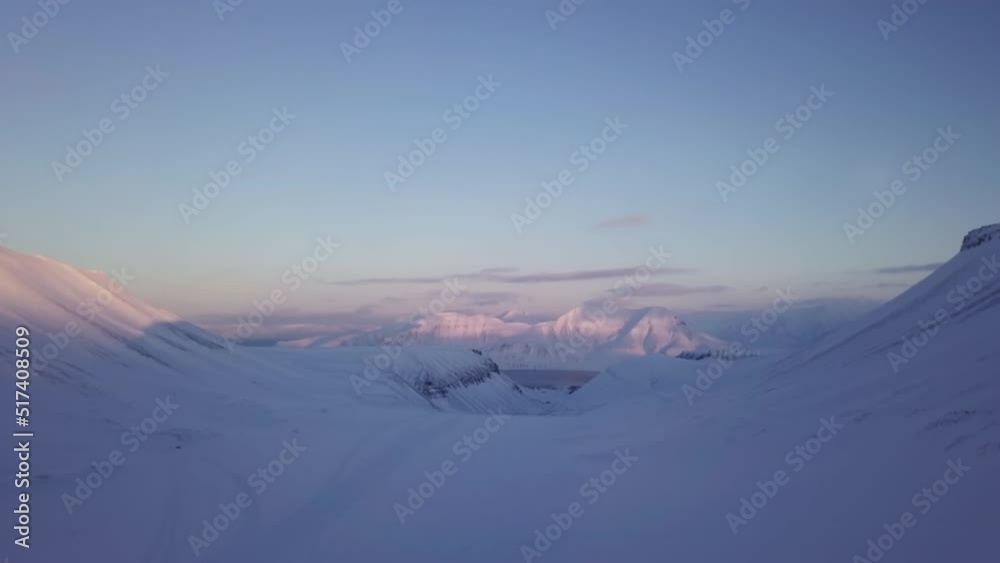 Drone flight near Longyearbyen The sun setting behind the snowy mountains on Svalbard. White snowy mountains
