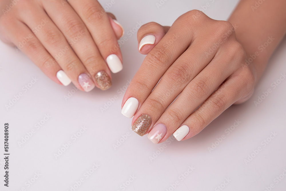 Beautiful female hands with romantic manicure nails, white and pink gel polish with golden glitter

